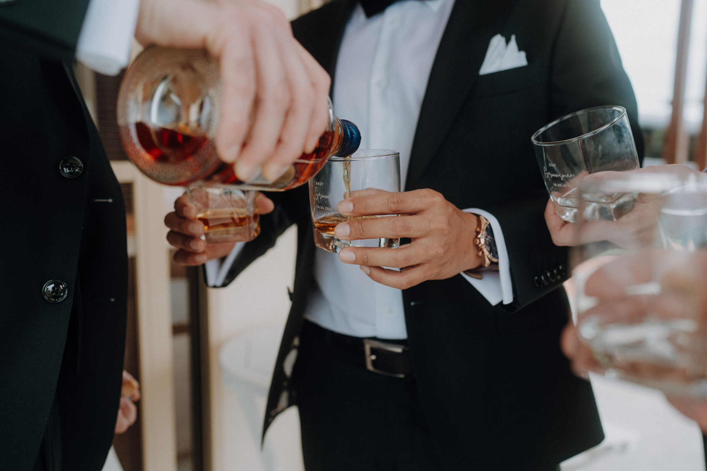 Several people in formal attire pour and hold glasses of whiskey.