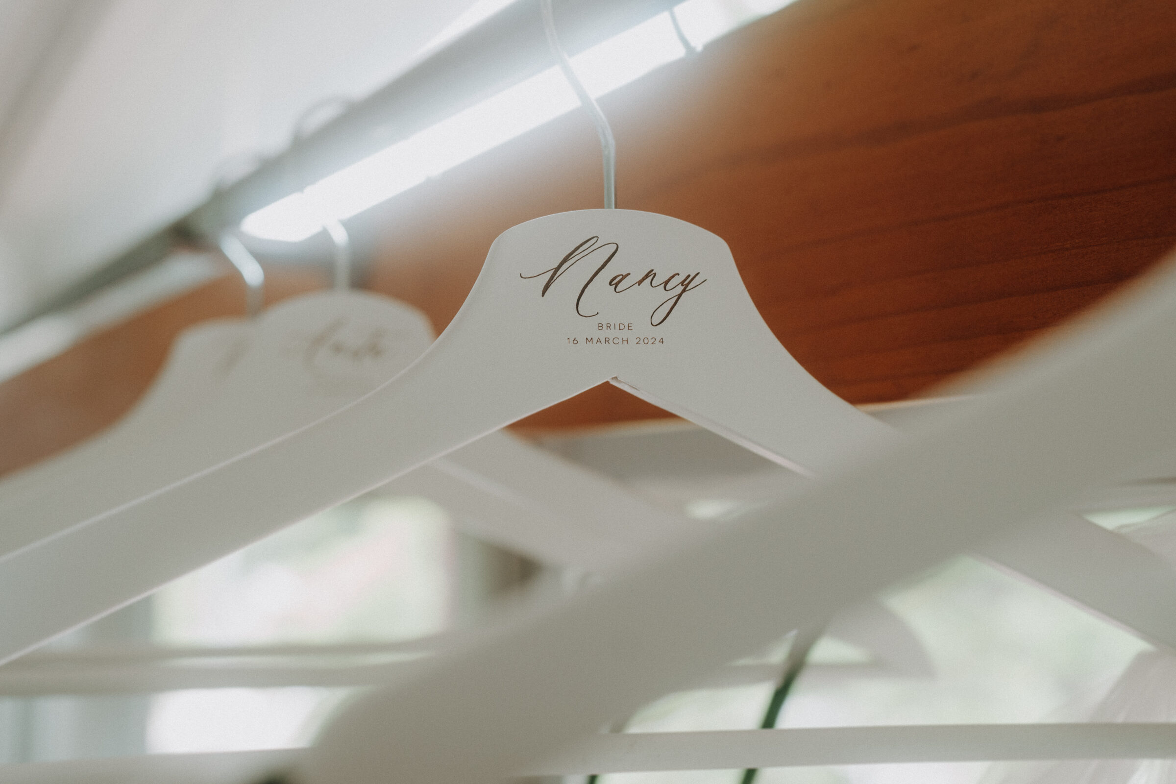 Close-up of white hangers on a rack, with "Nancy Bride 16 March 2024" written on one hanger.