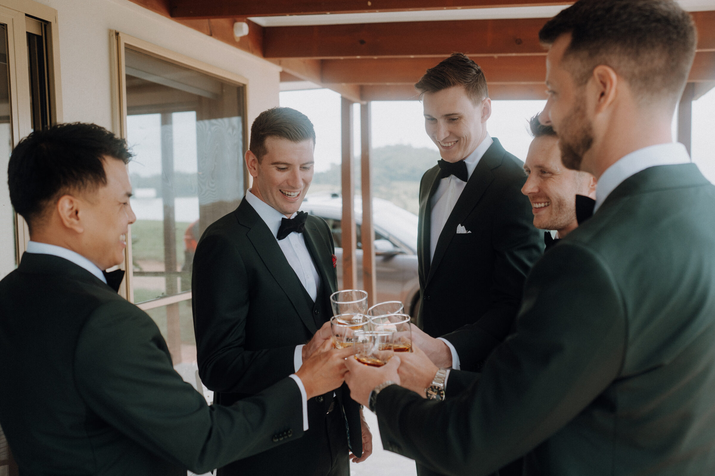 Five men in formal suits are standing outside, clinking glasses in a celebratory manner.