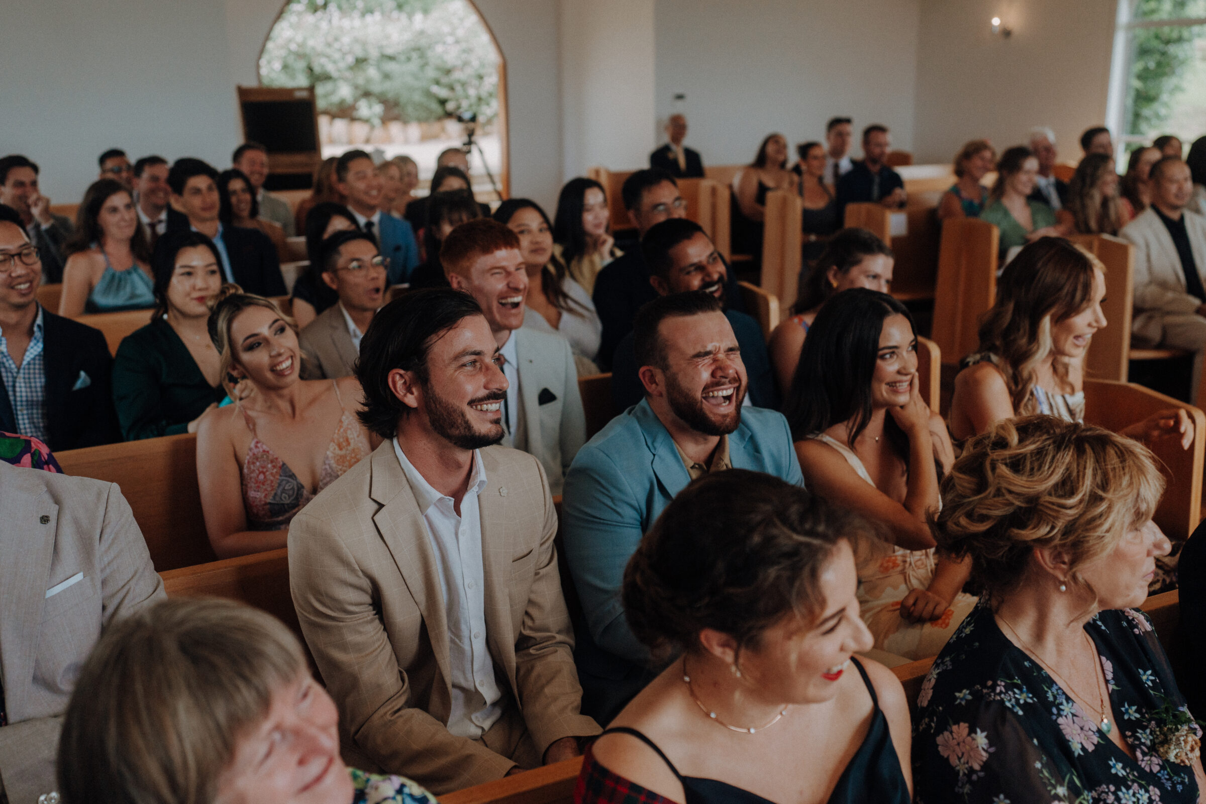 A group of people seated in a church, smiling and laughing during an event.