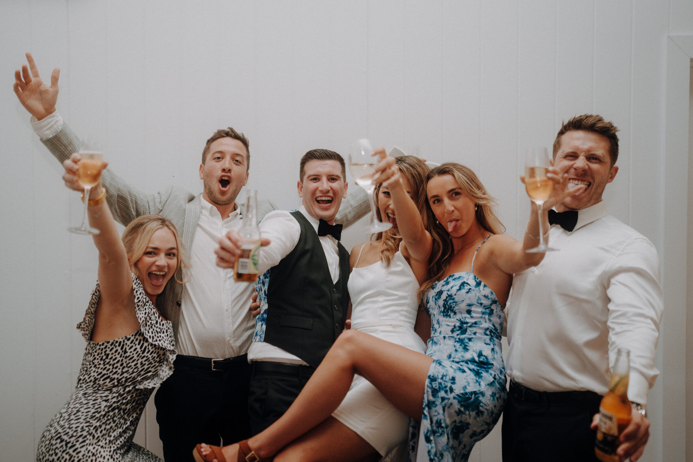 A group of six people in formal attire cheerfully pose with drinks, smiling and celebrating.