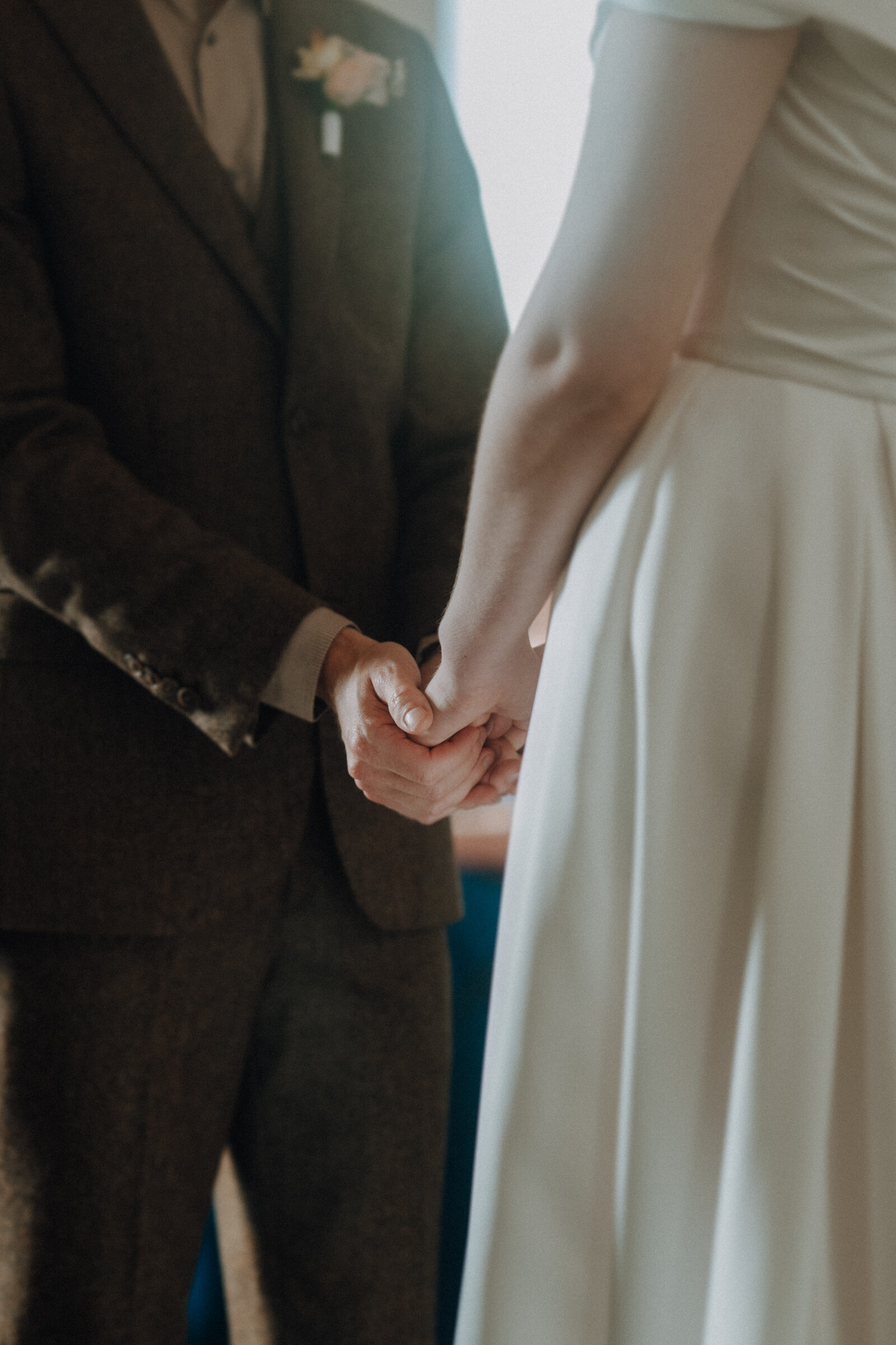 A couple dressed in formal attire hold hands, with the focus on their hands and torsos.