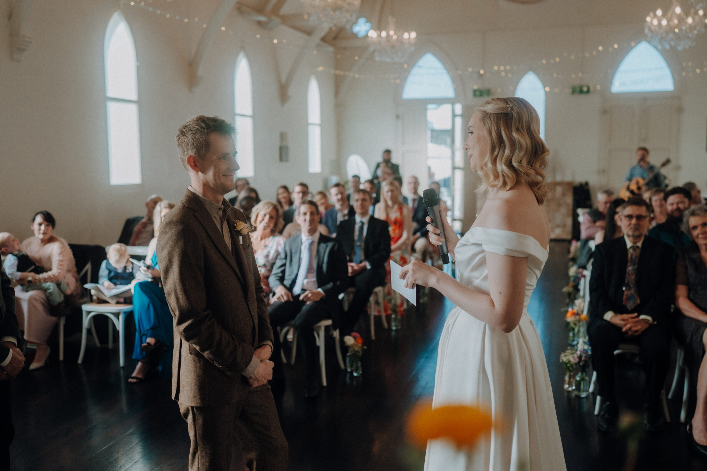 A bride and groom stand at the altar during a wedding ceremony in a decorated venue, with guests seated and observing.