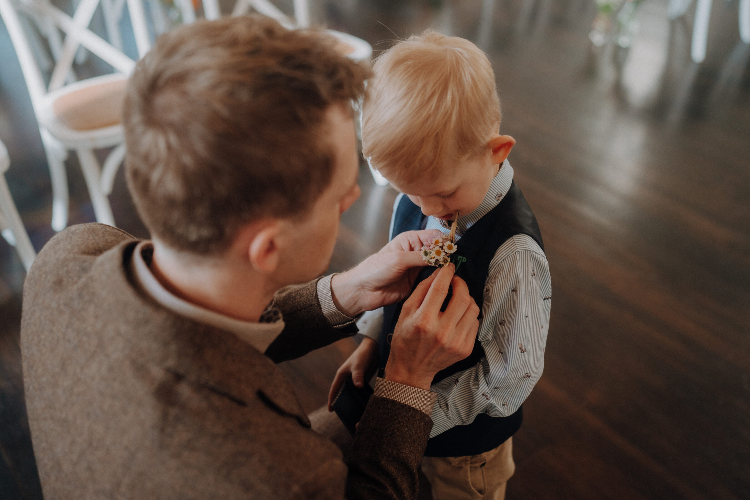 An adult helps a child adjust a boutonniere on his vest.