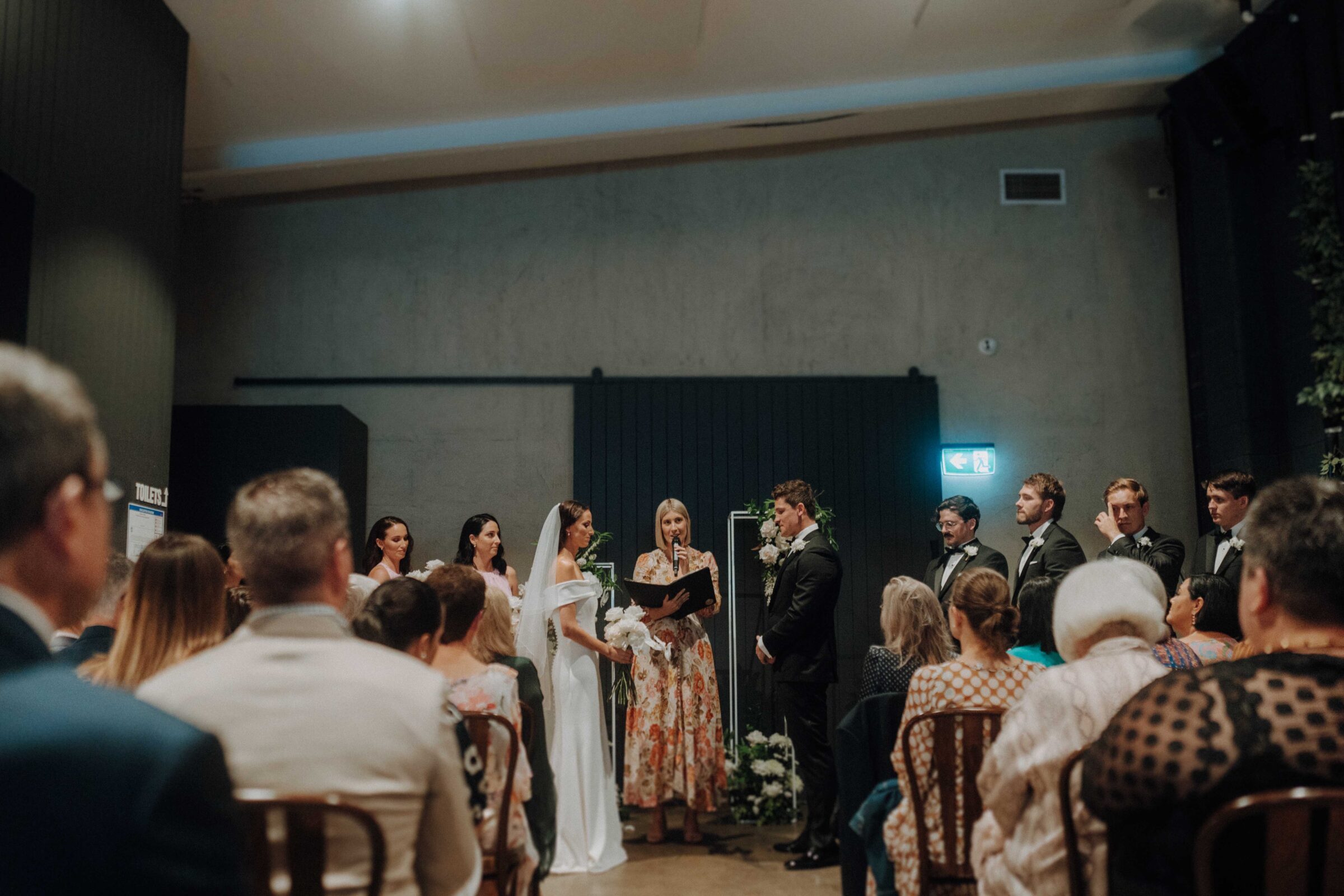 A bride and groom stand at the altar during a wedding ceremony, surrounded by bridesmaids and groomsmen, with guests seated in rows.