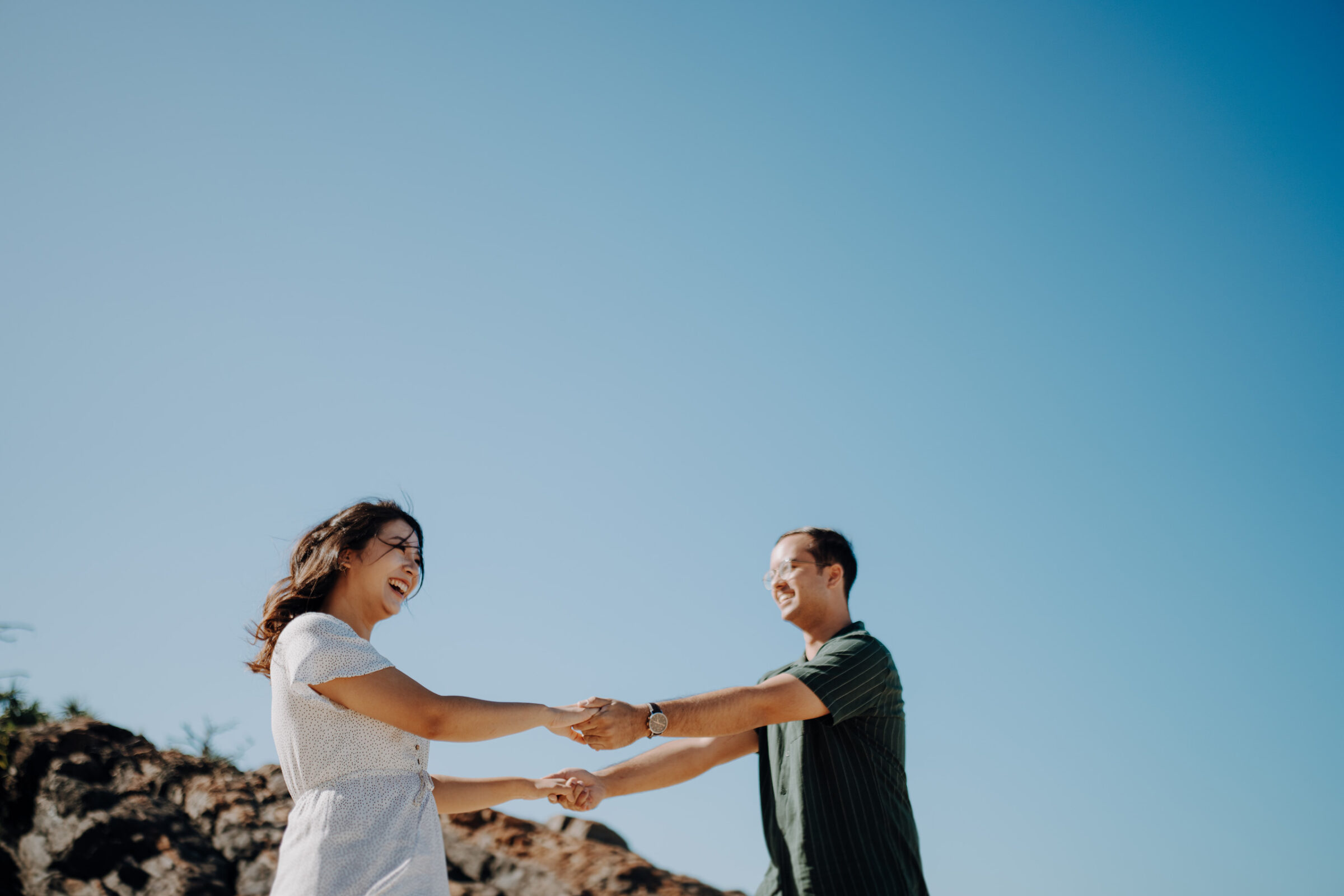 Two people are holding hands and smiling outdoors under a clear blue sky.