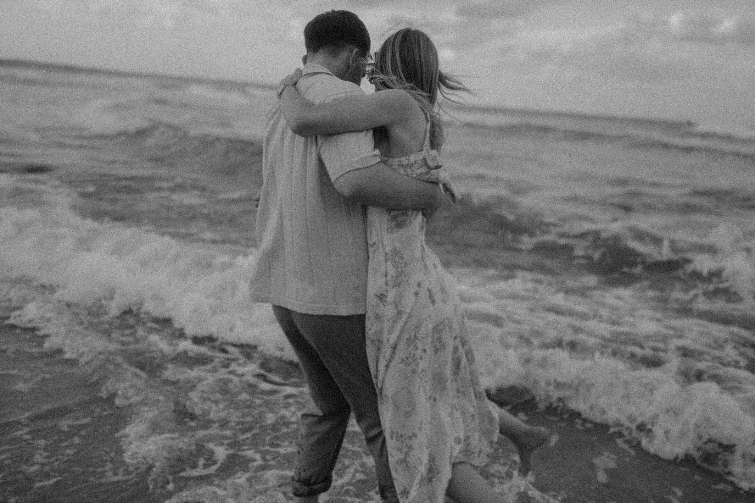 Couple embracing and walking along the shoreline, with waves gently crashing around them.