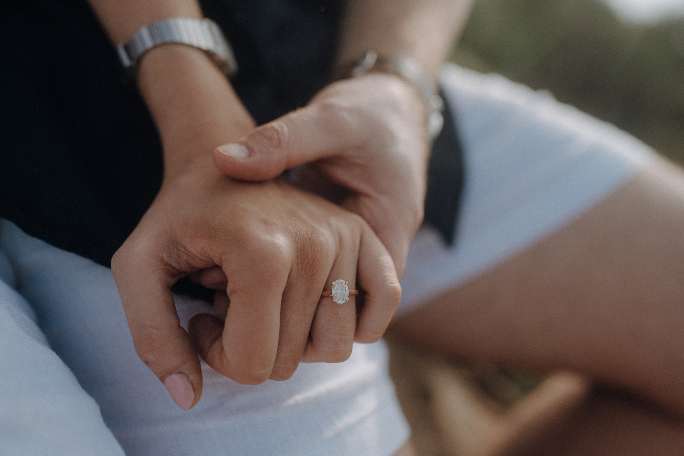 Two people holding hands, one wearing a ring with a large stone.