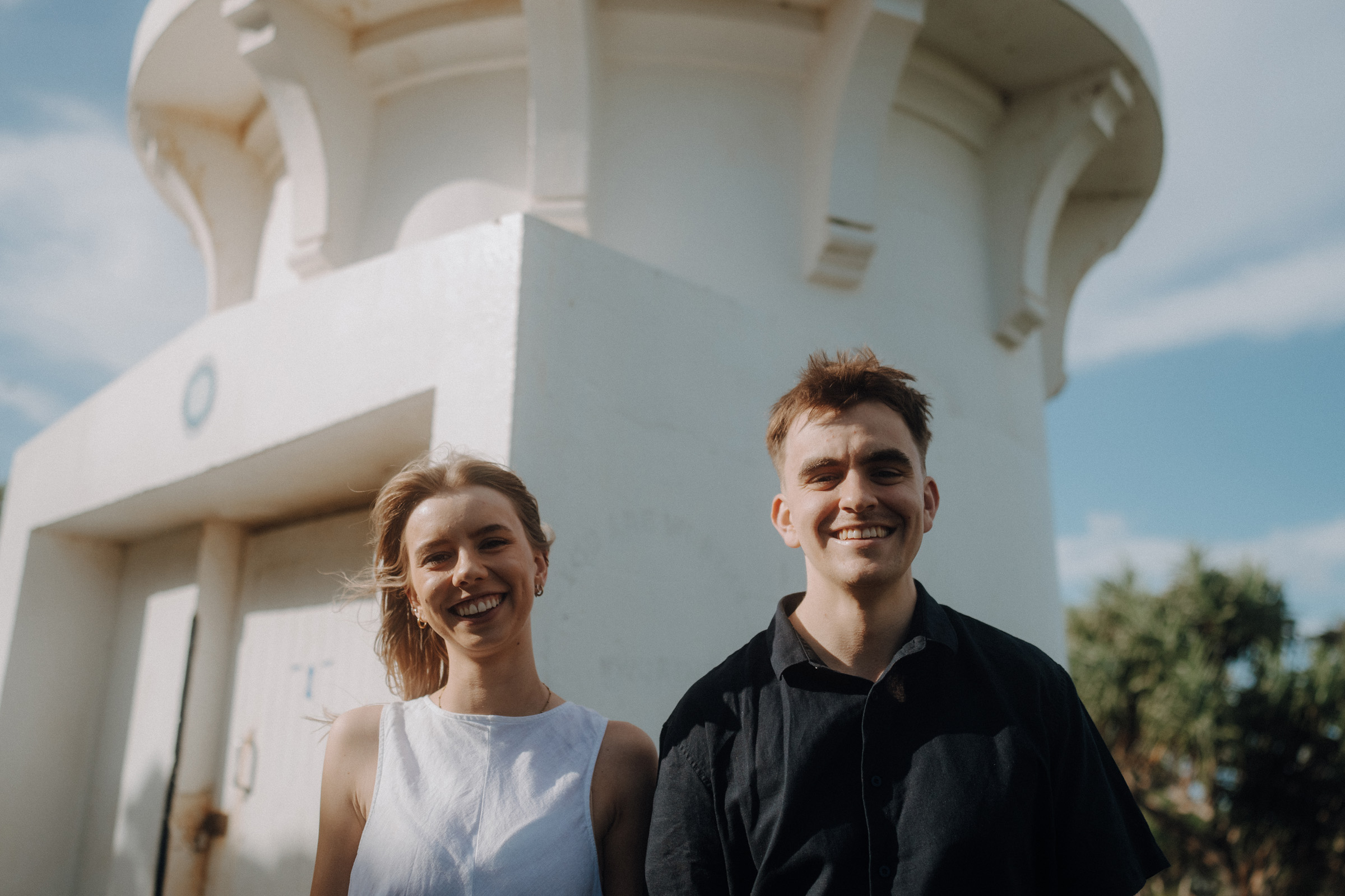 Two people standing in front of a white tower; the person on the left is wearing a white top, and the person on the right is wearing a black shirt.