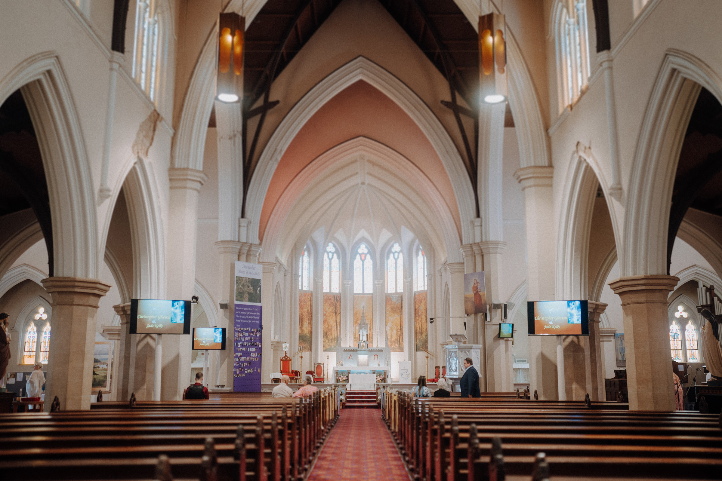 Interior of a church with high vaulted ceilings, wooden pews, stained glass windows, and a central altar.