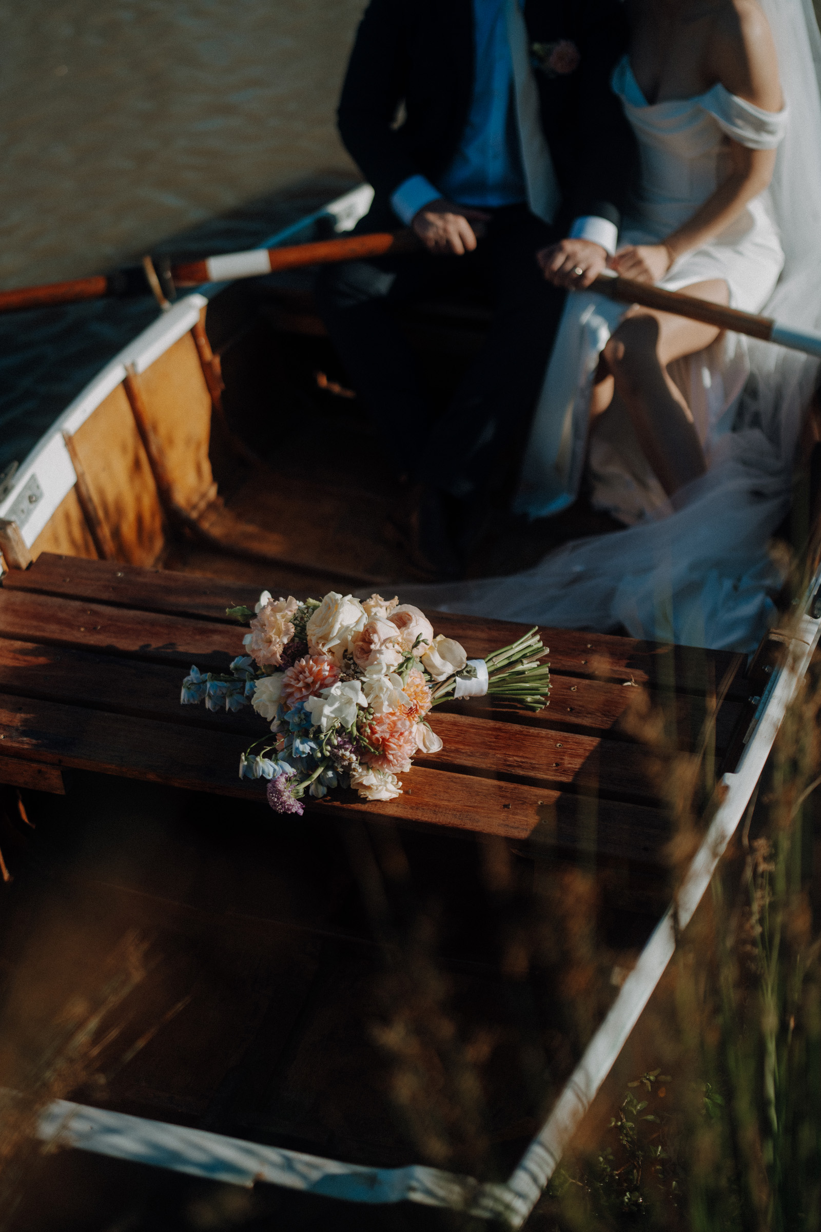 Bouquet of flowers in a rowboat with two seated people, one in a white dress and veil.