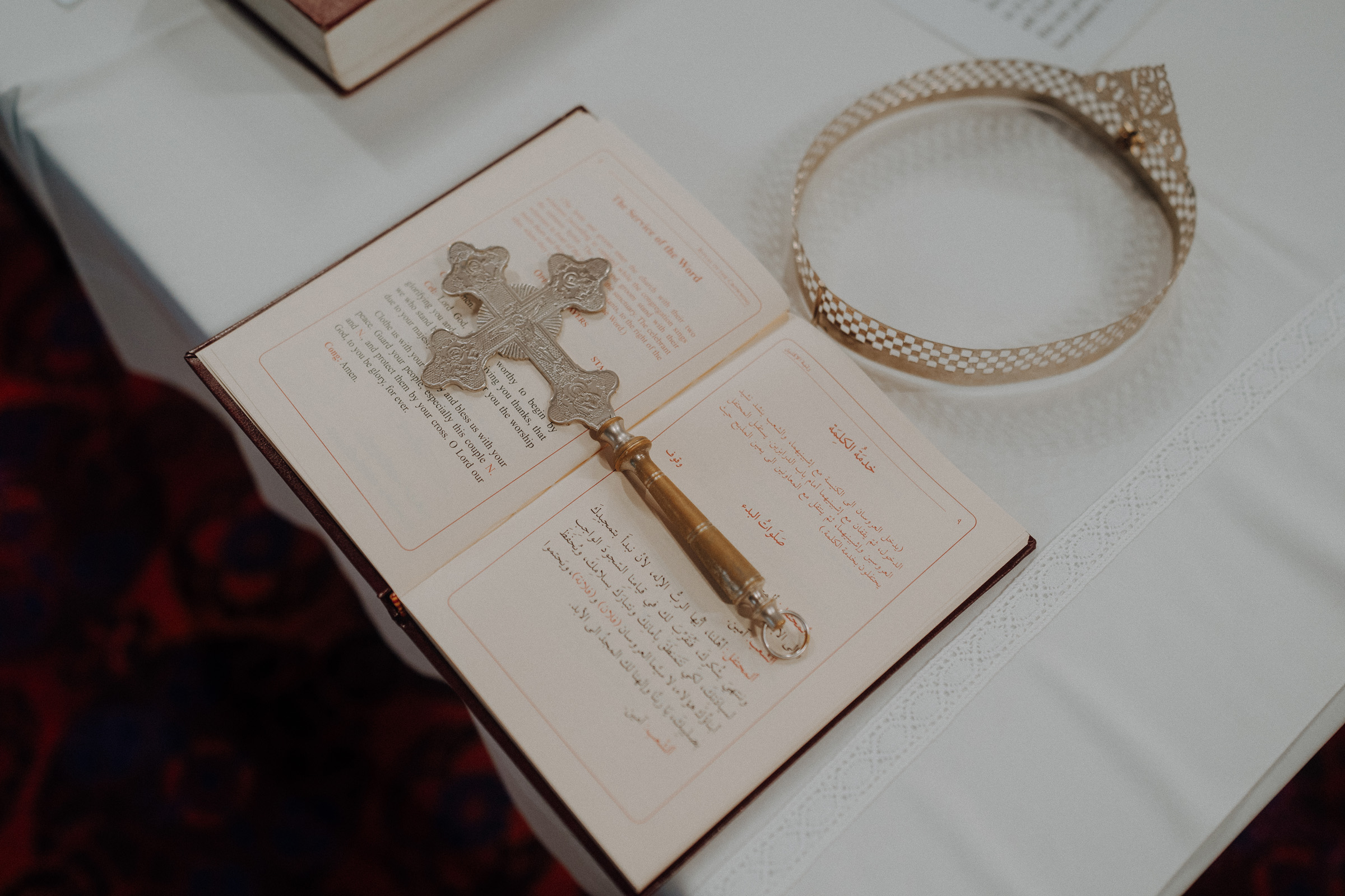 An open book with Arabic script, a decorative metallic cross on top, and an ornate circular metal headpiece are placed on a white cloth.